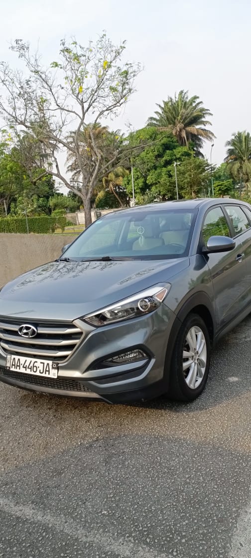 Hyundai Tucson: 60.000F CFA Véhicule SUV gris stationné sur une route avec des arbres en arrière-plan.