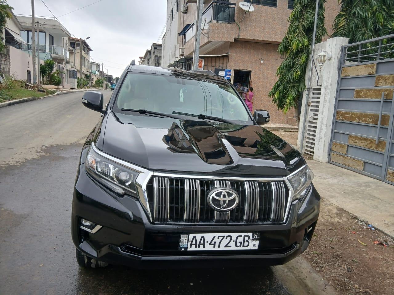 Toyota Land Cruiser Prado: 100.000F CFA SUV noir garé sur une route, avec un paysage urbain en arrière-plan.