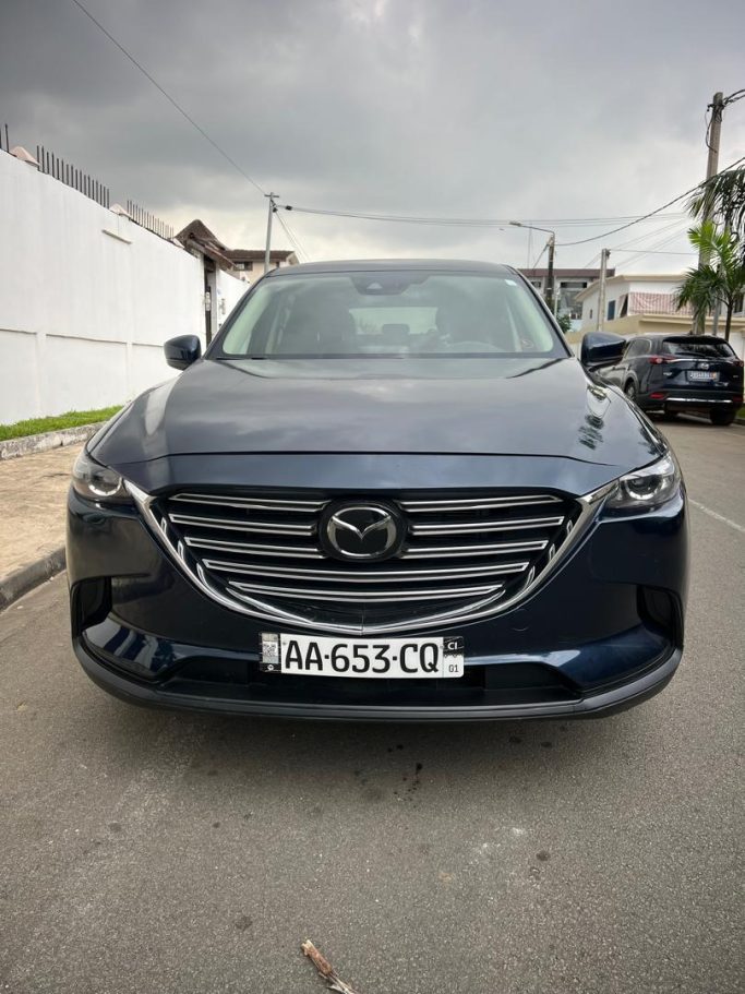 SUV - Mazda CX-9: 80.000F CFA Mazda noire garée sur une rue, vue de face avec un ciel nuageux en arrière-plan.